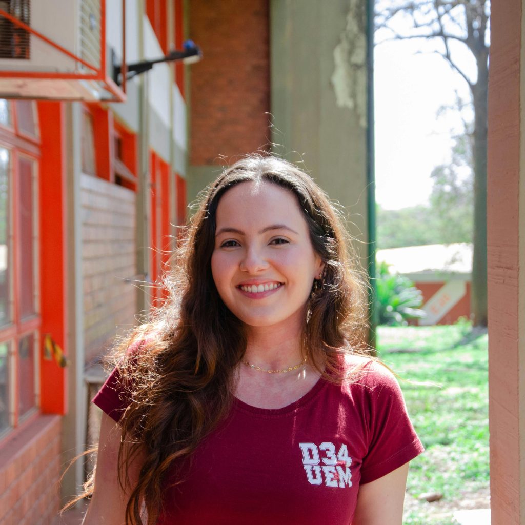Smiling young woman with long hair enjoying a sunny day on a university campus.