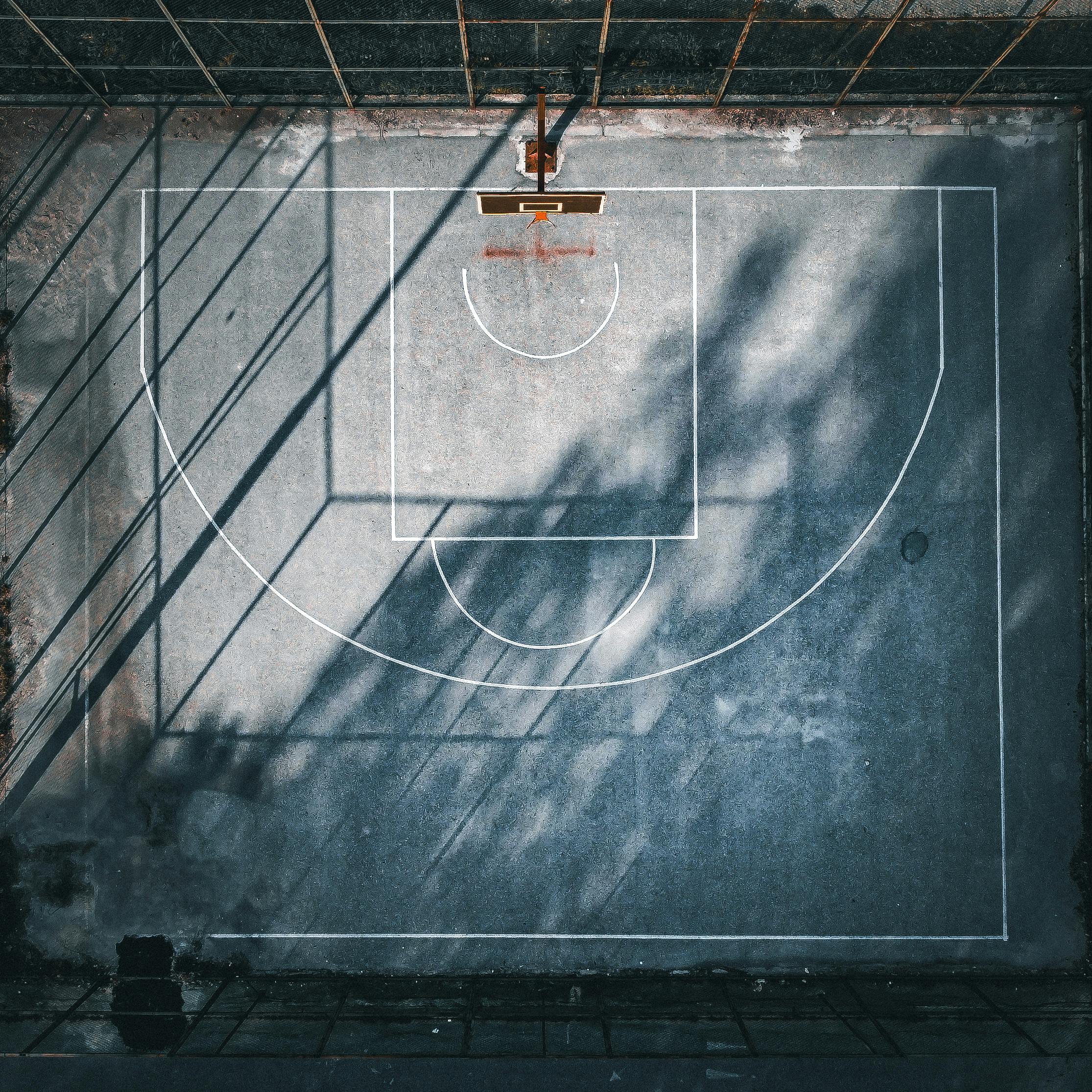 Aerial drone shot of a concrete basketball court with strong shadows.