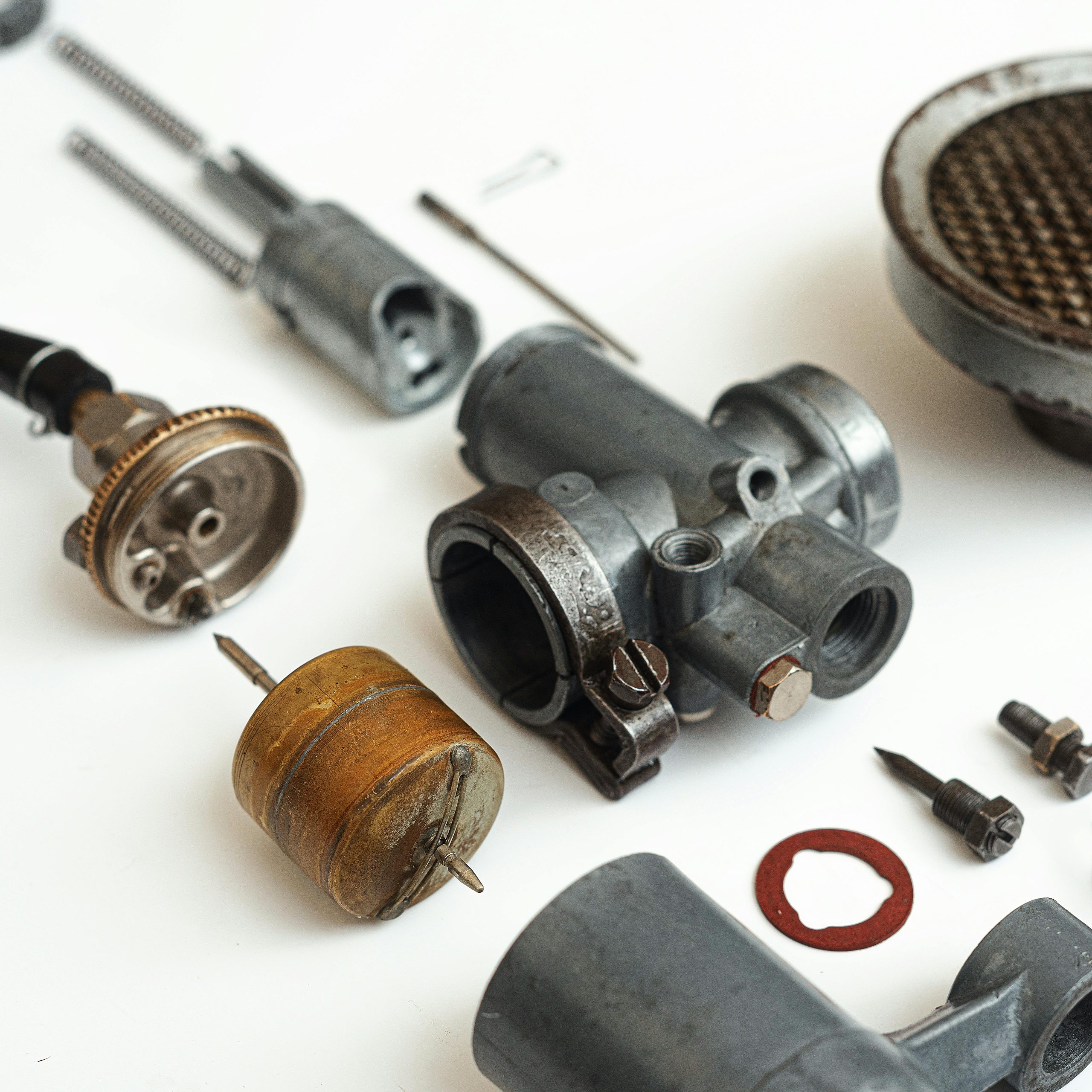 Detailed image of various carburetor components arranged on a white surface, showcasing industrial machinery elements.